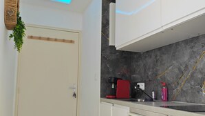 Una cuina moderna amb armaris blancs, un respatller de marbre i un sostre amb il·luminació LED blava.