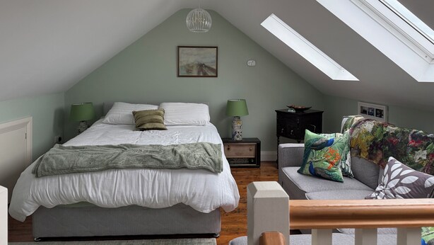 A bedroom with a bed, two bedside lamps, a nightstand, a sofa, a decorative bowl, a painting, and skylights.