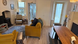 A living room with a fireplace, yellow sofa, wooden dining table, and a view of the outside.
