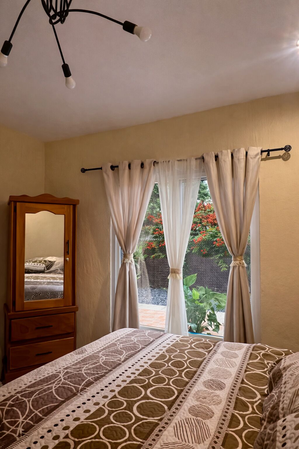 Een slaapkamer met een bed, een houten garderobe, een spiegel en een raam met gordijnen.
