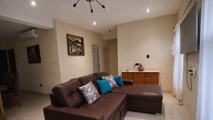 A living room with a brown leather sofa, a wooden cabinet, a flat-screen TV, and a painting on the wall.