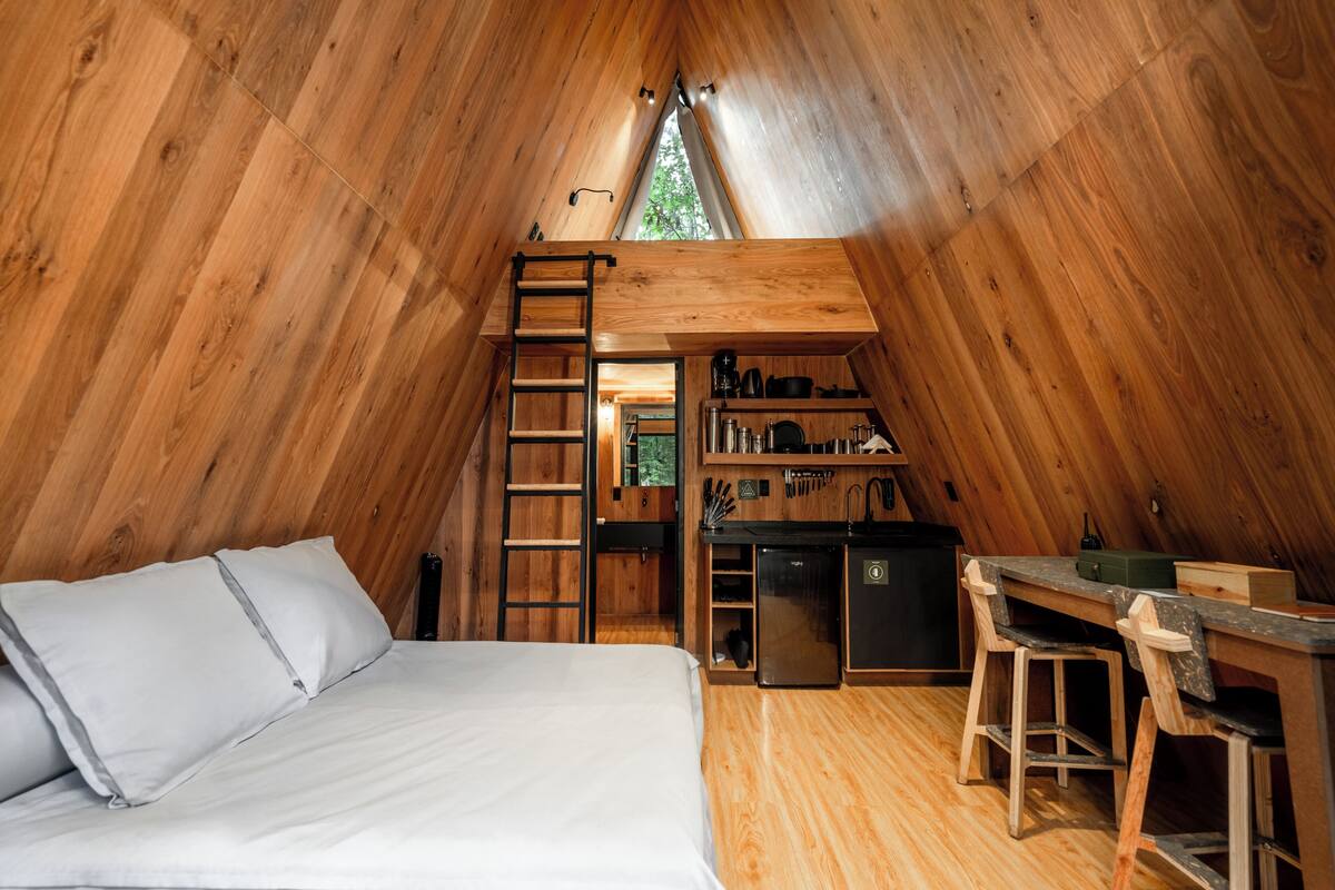 Un intérieur chaleureux, avec des murs en bois, un lit en mezzanine, un bureau et un coin cuisine.
