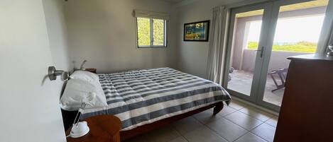 A bedroom with a bed, a nightstand, a dresser, a window, and a door leading to a balcony.