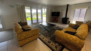 Sala de estar com sofás estampados, televisão de tela plana, lareira e grandes portas de vidro deslizantes para um jardim.