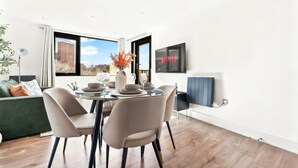 Ein moderner Essbereich mit Tisch für vier Personen, einem grünen Sofa und einem großen Fenster mit Blick auf ein Gebäude.
