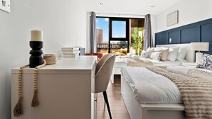 Ein Hotelzimmer mit Bett, Schreibtisch, Stuhl, Nachttisch, Lampe und Blick ins Freie.