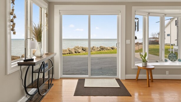 A room with a view of the ocean, a sliding glass door, a small table with a plant, and a console table with a lamp. - Waterfront | 4 guests | 1 bedroom | 2 beds | 2 full baths (Hilton)