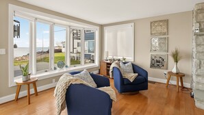 A living room with large windows, a blue sofa, a small table, and decorative wall art. - Waterfront | 4 guests | 1 bedroom | 2 beds | 2 full baths (Hilton)