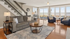 A modern living room with a staircase, a sofa, two armchairs, a coffee table, and a view of the sea. - Waterfront | 4 guests | 1 bedroom | 2 beds | 2 full baths (Hilton)
