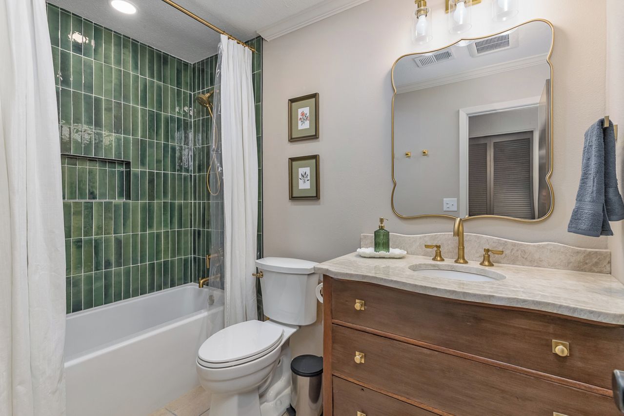 Une salle de bain avec une baignoire, des toilettes, un meuble-lavabo avec un miroir et des tableaux encadrés au mur.