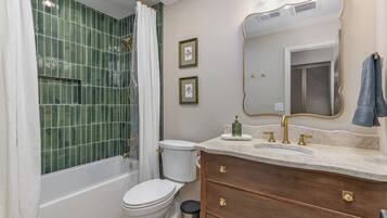Une salle de bain avec une baignoire, des toilettes, un meuble-lavabo avec un miroir et des tableaux encadrés au mur.