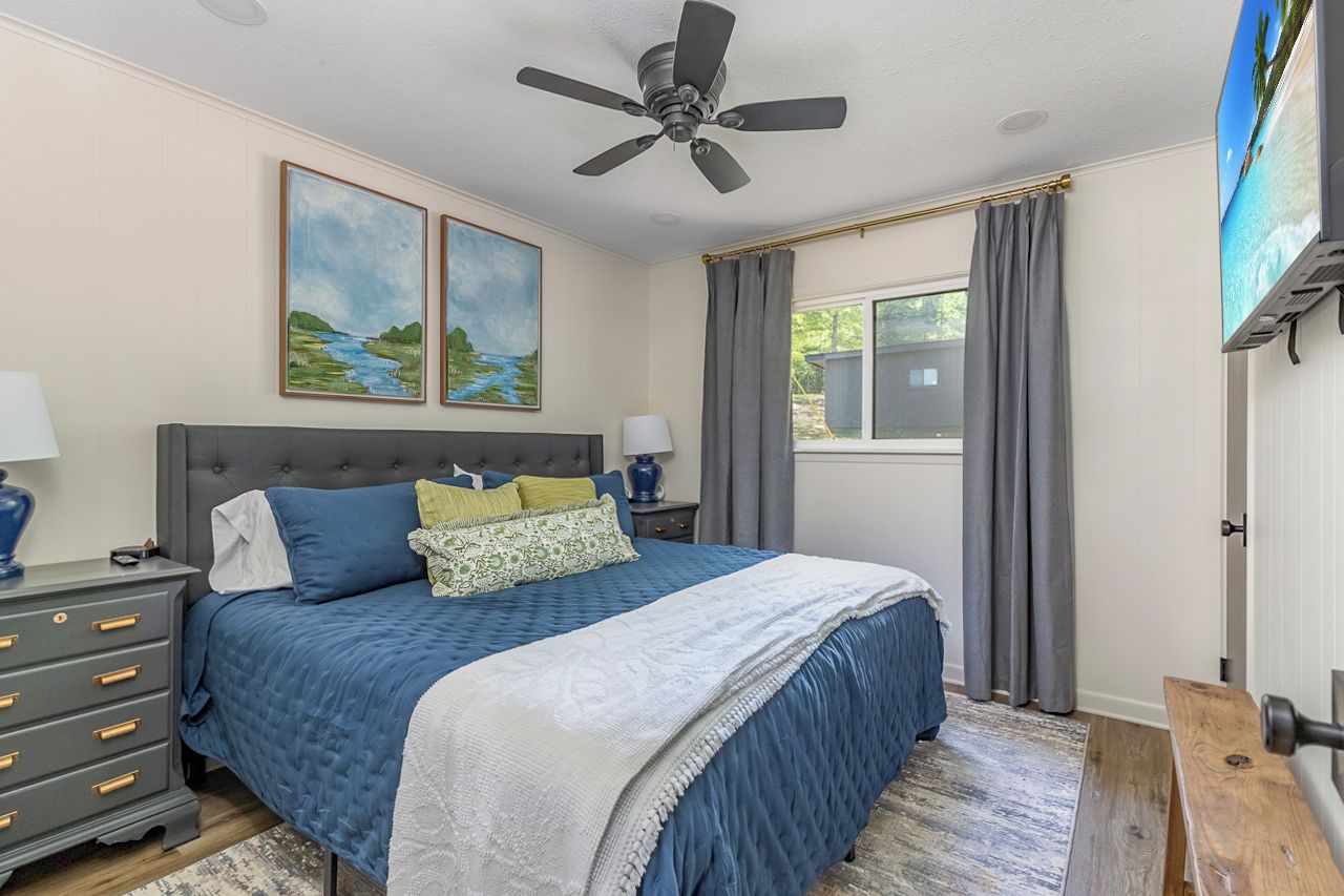 A bedroom with a bed, a nightstand, a ceiling fan, and a window with curtains.