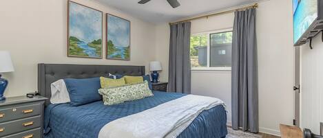 A bedroom with a bed, a nightstand, a ceiling fan, and a window with curtains.