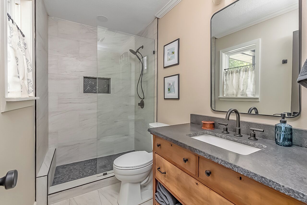 Un baño moderno con cabina de ducha de vidrio, inodoro blanco, tocador con lavamanos y un espejo grande.