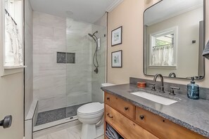 Une salle de bain moderne avec une douche à parois de verre, des toilettes blanches, un meuble-lavabo et un grand miroir.