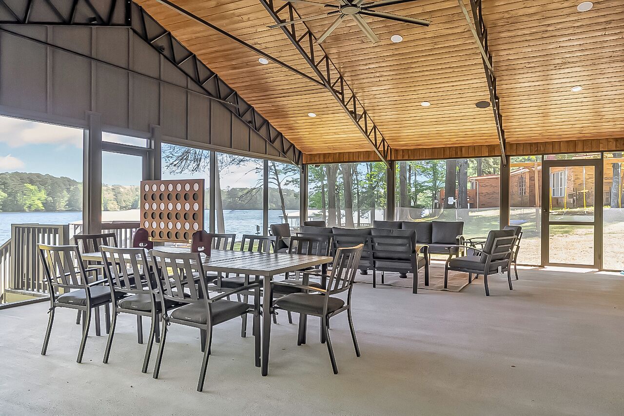 A covered outdoor seating area with tables and chairs, large windows, and a view of the lake.