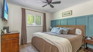A bedroom with a bed, a ceiling fan, a dresser, a window with curtains, and a wall-mounted TV.
