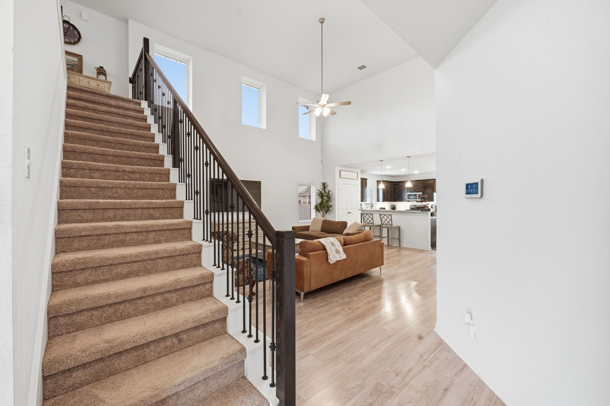 A staircase with carpeted steps and black railings leading to a living area with a sofa and a ceiling fan.