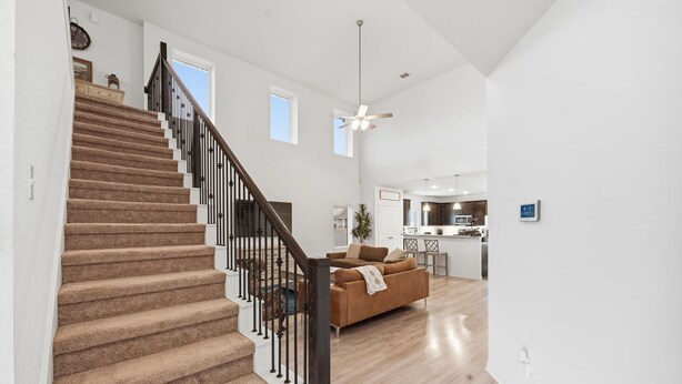 Eine Treppe mit Teppichstufen und schwarzen Geländern führt zu einem Wohnbereich mit Sofa und Deckenventilator.