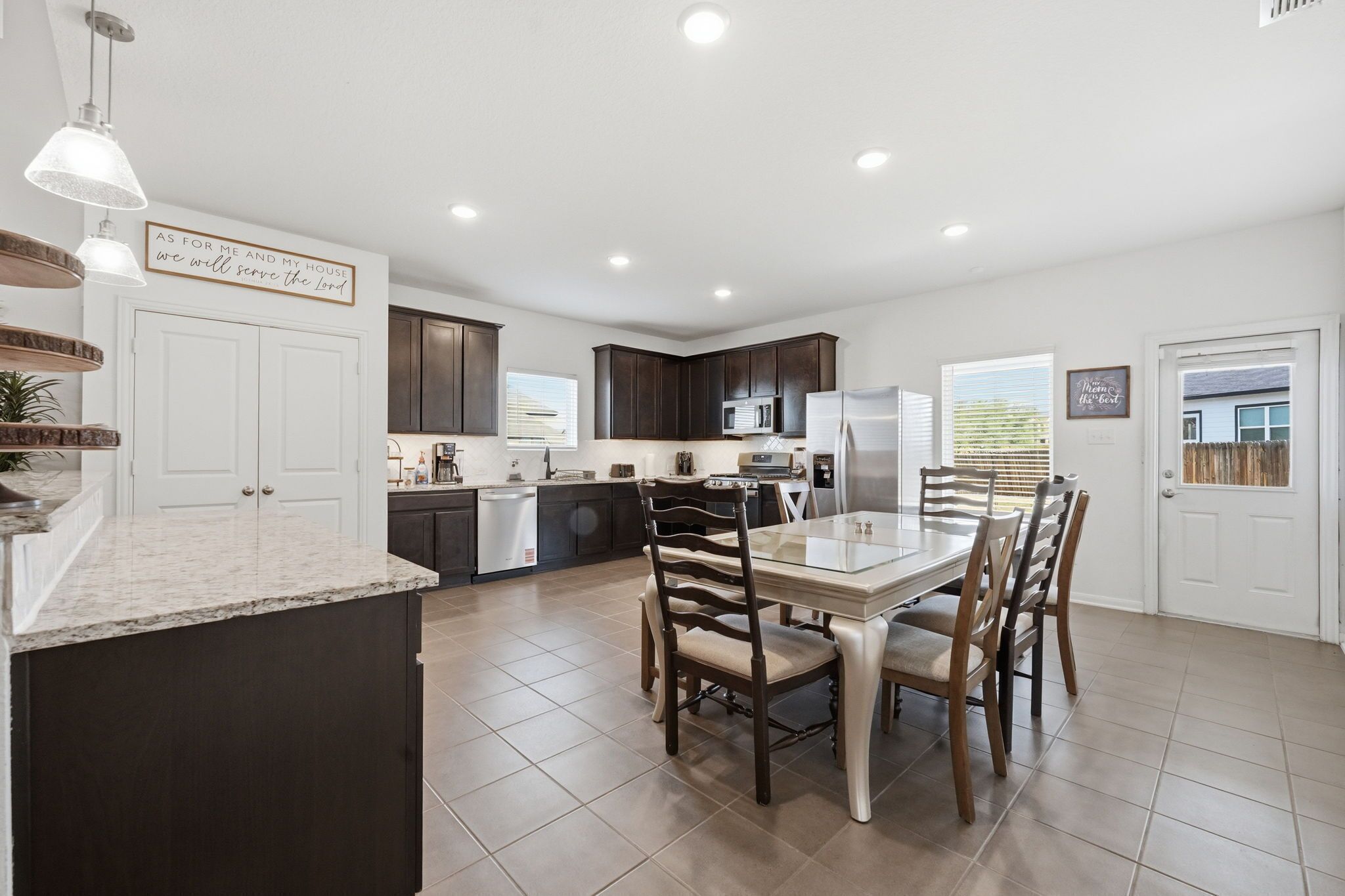 A modern kitchen with dark cabinets, a central island, and a dining area with a table and chairs.