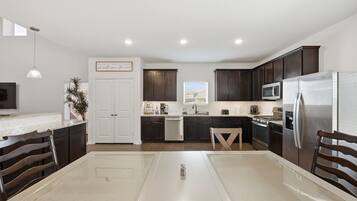 A modern kitchen with dark cabinets, stainless steel appliances, a dining area with a table and chairs, and a pendant light.
