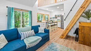 A modern interior with a blue sofa, wooden staircase, kitchen area, and large windows. - The Palm Loft Retreat W/ Ground Floor Walkout Patio 🏝️ (Palm Bay)