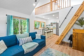 A modern interior with a blue sofa, wooden staircase, kitchen area, and large windows. - The Palm Loft Retreat W/ Ground Floor Walkout Patio 🏝️ (Palm Bay)