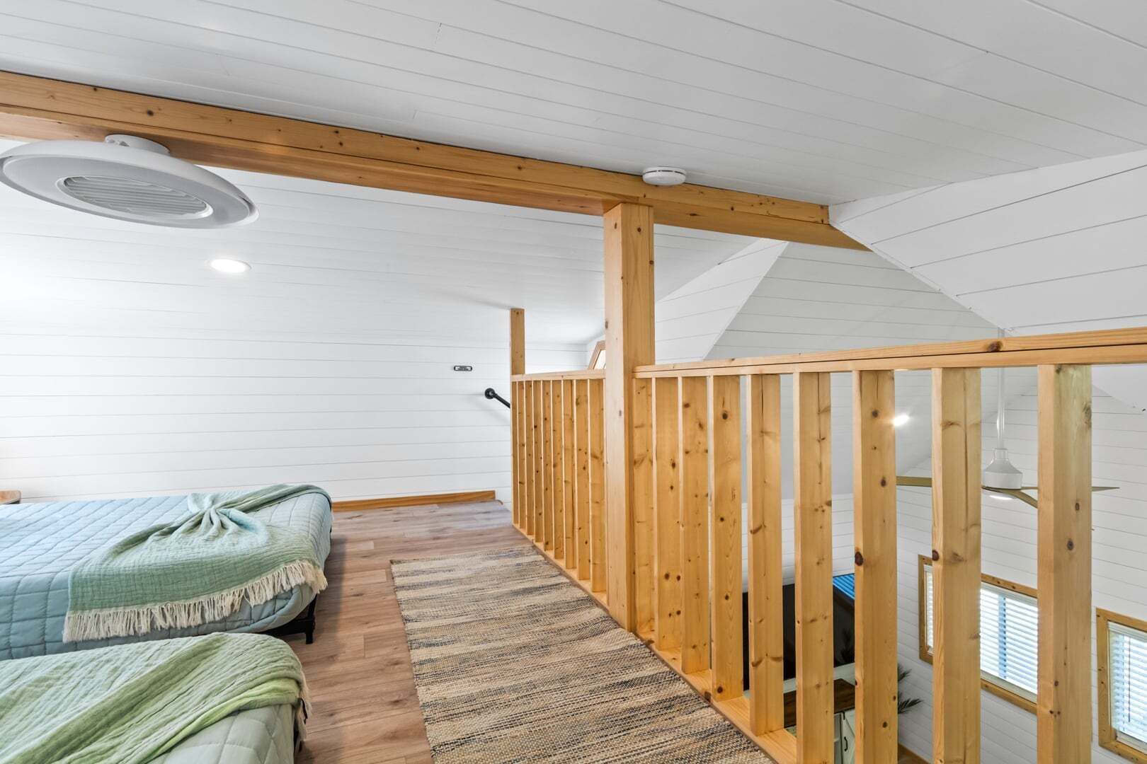 A room with a bed, a wooden railing, a ceiling fan, and a window.