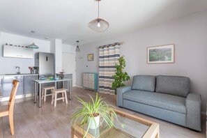 A modern living room with a sofa, a dining table, and a kitchen area in the background. - Appartement charmant à Aix-en-Provence - Nomad by Welkeys (Aix-en-Provence)