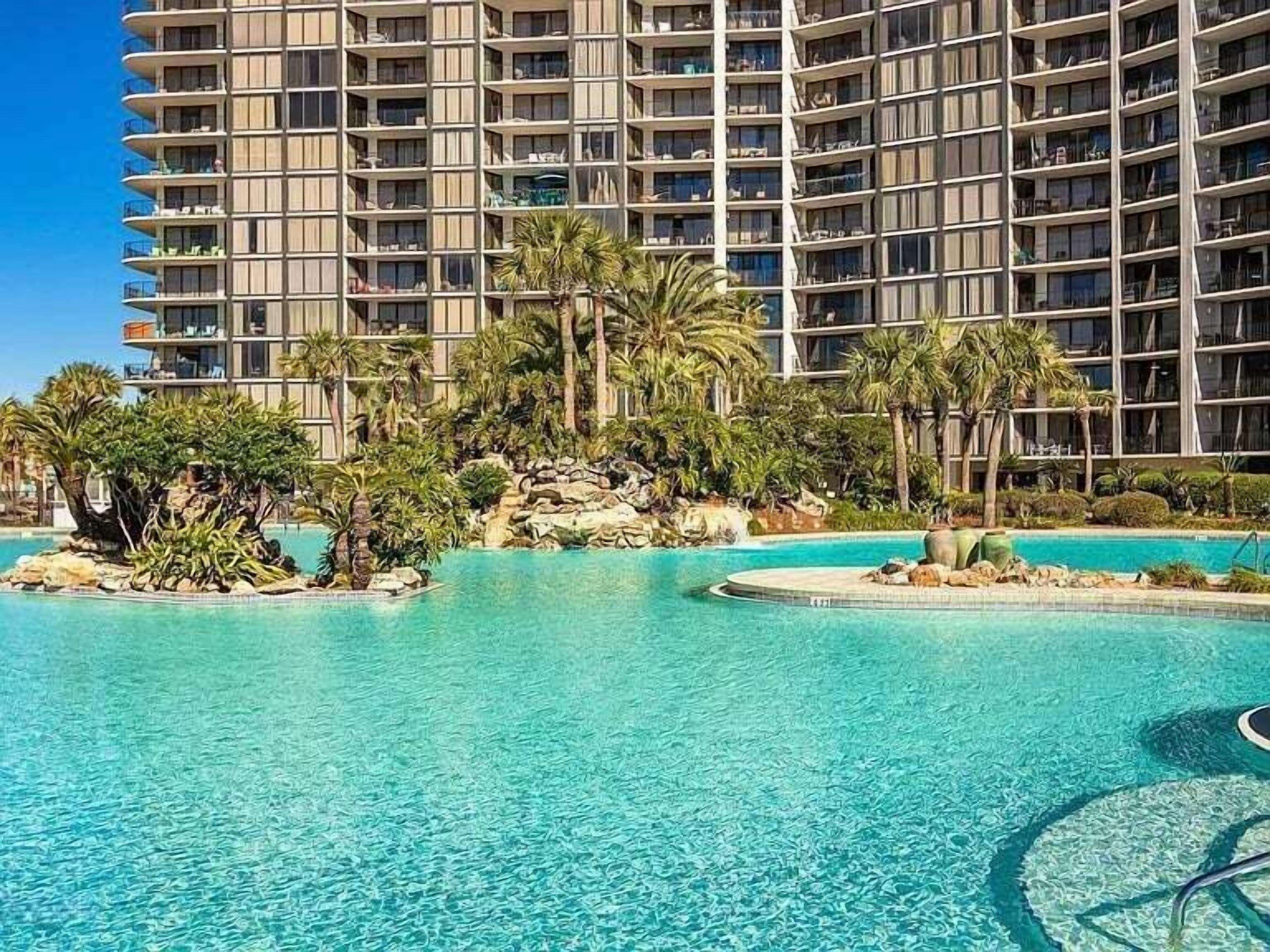 Ein Hotel mit einem großen Pool, umgeben von Palmen und einer Felseninsel.