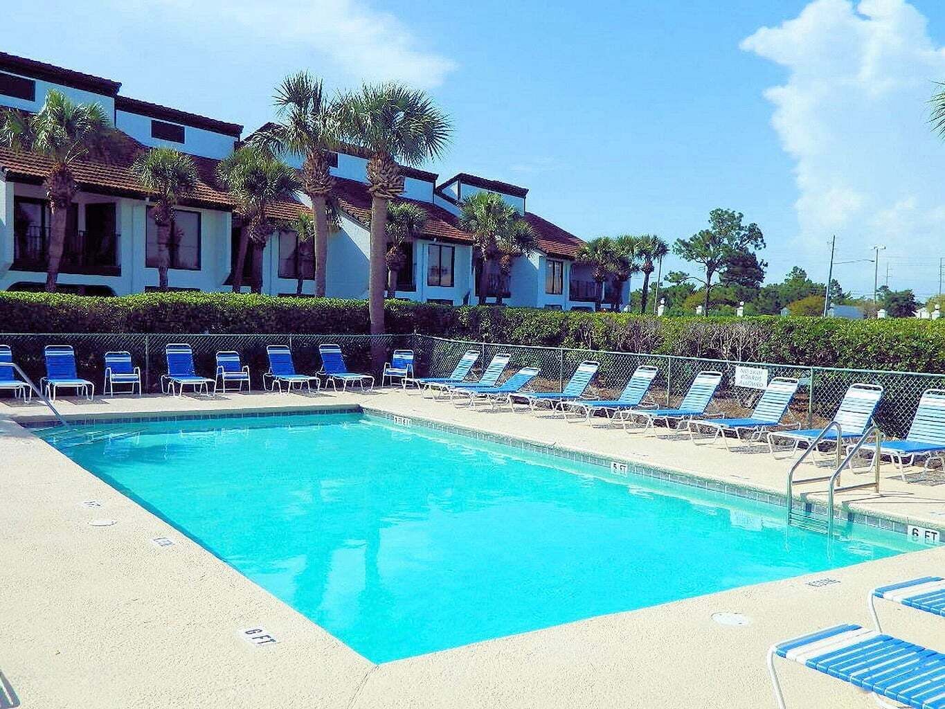 A swimming pool with blue chairs, a fence, and buildings in the background.