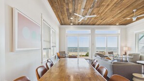 A spacious room with a wooden ceiling, large windows with ocean views, a long wooden table, and comfortable seating. - Pink Sands 1492-Gulf Front Pool-Sleeps 20 (Port Saint Joe)