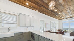 A modern kitchen with white cabinets, a large island, and a view of the ocean. - Pink Sands 1492-Gulf Front Pool-Sleeps 20 (Port Saint Joe)