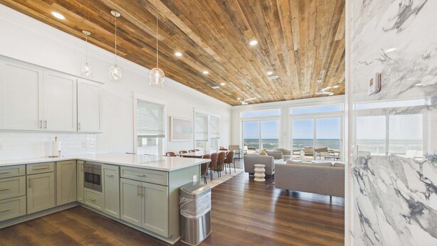 A modern kitchen with wooden ceiling, large windows, and a view of the ocean. - Pink Sands 1492-Gulf Front Pool-Sleeps 20 (Port Saint Joe)