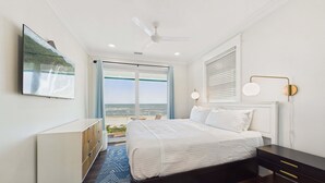 A bedroom with a bed, a dresser, a ceiling fan, a TV, and a view of the ocean. - Pink Sands 1492-Gulf Front Pool-Sleeps 20 (Port Saint Joe)