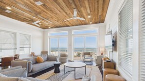 A spacious living area with a large window overlooking the ocean, a ceiling fan, and a modern interior design. - Pink Sands 1492-Gulf Front Pool-Sleeps 20 (Port Saint Joe)