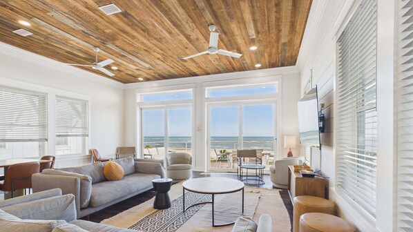 A spacious living area with a large window overlooking the ocean, a ceiling fan, and a modern interior design.