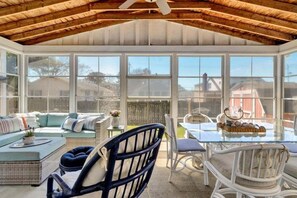 Eine überdachte Terrasse mit Glasveranda, Korbmöbeln und einem Tisch mit einer Korbablage.