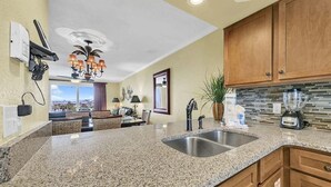 A kitchen with granite countertops, a double sink, wooden cabinets, a blender, and a view through the window. - 🦩Book Me Baby! Pinkie's Island Oasis🦩 (Destin)