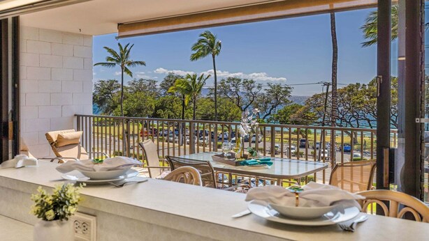 A balcony with a table set for dining, overlooking a parking area and palm trees. - New Listing! Steps to the beach in Kihei (Kihei)
