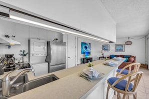 A modern kitchen with stainless steel appliances, a central island with seating, and a dining area with a sofa and chairs. - New Listing! Steps to the beach in Kihei (Kihei)