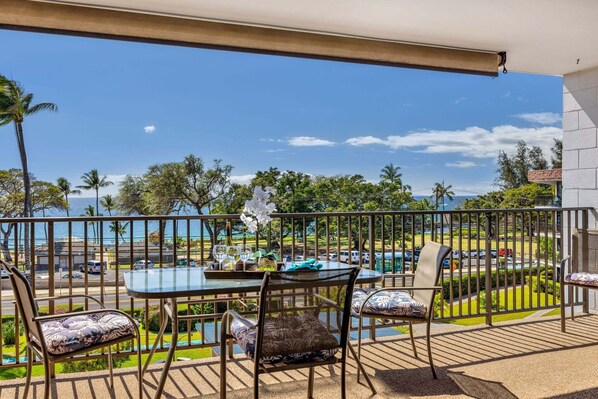 A balcony with a table and chairs, a view of the ocean, and a clear sky. - New Listing! Steps to the beach in Kihei (Kihei)