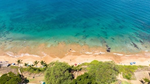 Luftaufnahme eines Strandes mit klarem türkisblauem Wasser, Sandstrand und etwas Grün.