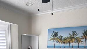 Een netjes opgemaakt bed met een gewatteerde sprei, een schilderij van palmbomen aan de muur en een witte wandplank.