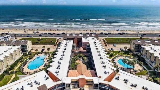 Een hotel met meerdere zwembaden, uitzicht op het strand en een parkeerplaats.