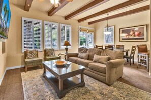 A living room with a sofa, coffee table, and dining area with chairs. - Villa Sunstone A | 1BR Legacy Villa (La Quinta)