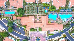 Une vue aérienne d’un complexe hôtelier comprenant plusieurs bâtiments, des piscines et une place centrale circulaire.