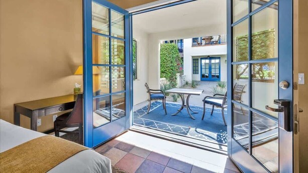 Une chambre d’hôtel équipée d’un lit, d’un bureau et offrant une vue sur une terrasse extérieure avec une table et des chaises.