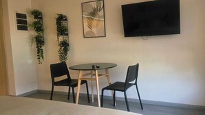 Een kamer met een bed, een ronde tafel met twee stoelen, een aan de muur bevestigde televisie en een raam met gordijn.