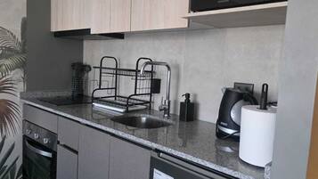 A modern kitchen with a stainless steel sink, black kettle, and a dish rack.